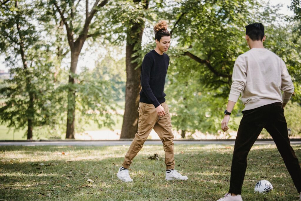 Two young men enjoying a casual soccer game in a sunny park setting.